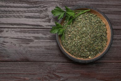 Photo of Dried aromatic parsley and fresh leaves in plate on wooden table, top view. Space for text