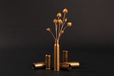 Photo of Bullet cases with beautiful dry plant on black background