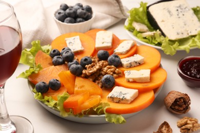 Photo of Delicious persimmon with blue cheese, blueberries, lettuce and walnuts on white table, closeup