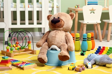 Photo of Teddy bear on light blue baby potty and many other toys in room. Toilet training