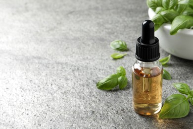 Photo of Glass bottle of basil essential oil and leaves on grey stone table. Space for text