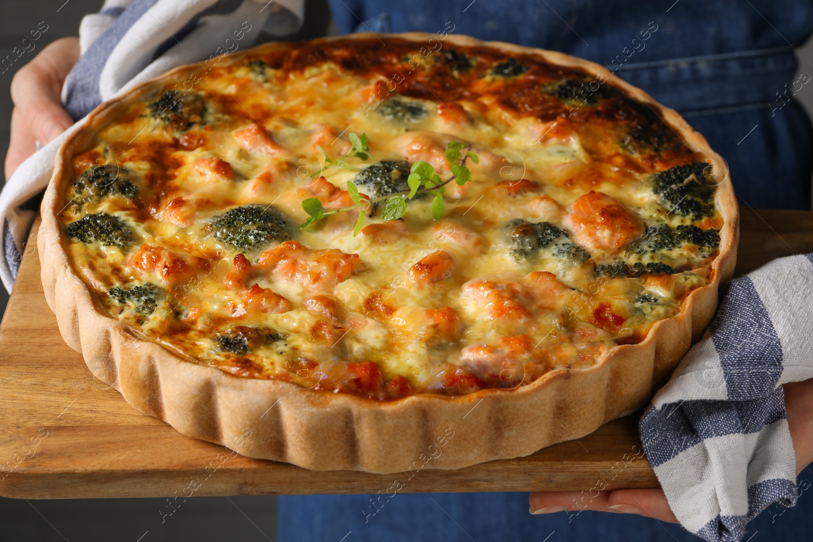 Photo of Woman holding wooden board with delicious homemade salmon quiche, closeup