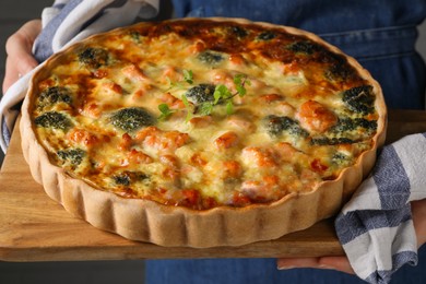 Woman holding wooden board with delicious homemade salmon quiche, closeup