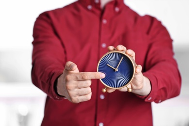 Young man holding alarm clock on blurred background. Time concept