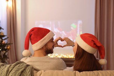 Couple making heart with hands near video projector in room. Christmas atmosphere