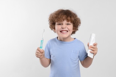 Photo of Cute little boy holding electric toothbrush and tube of toothpaste on white background. Space for text