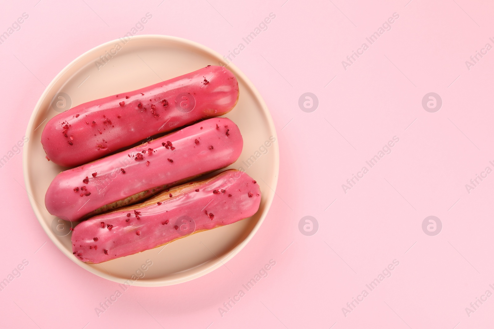 Photo of Delicious eclairs covered with glaze on pink background, top view. Space for text