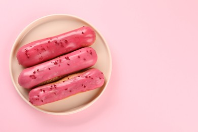 Photo of Delicious eclairs covered with glaze on pink background, top view. Space for text