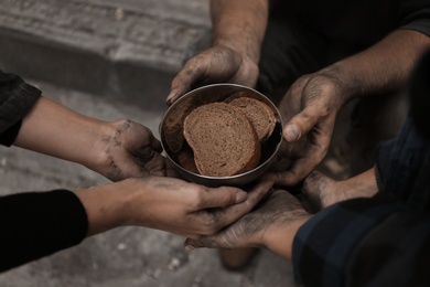 Photo of Poor homeless people with pieces of bread outdoors, closeup
