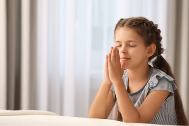 Cute little girl with hands clasped together saying bedtime prayer at home. Space for text