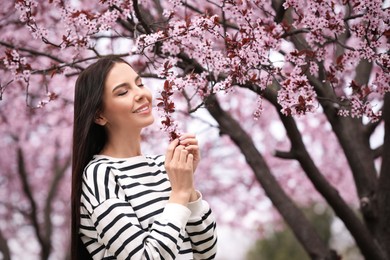 Pretty young woman near blooming tree in park. Spring look