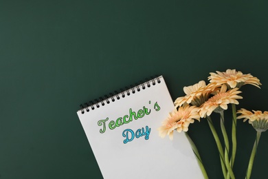 Photo of Notebook with phrase Teacher's Day and beautiful flowers on green chalkboard, flat lay. Space for text