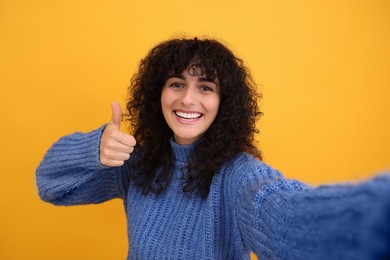 Beautiful young woman taking selfie on orange background