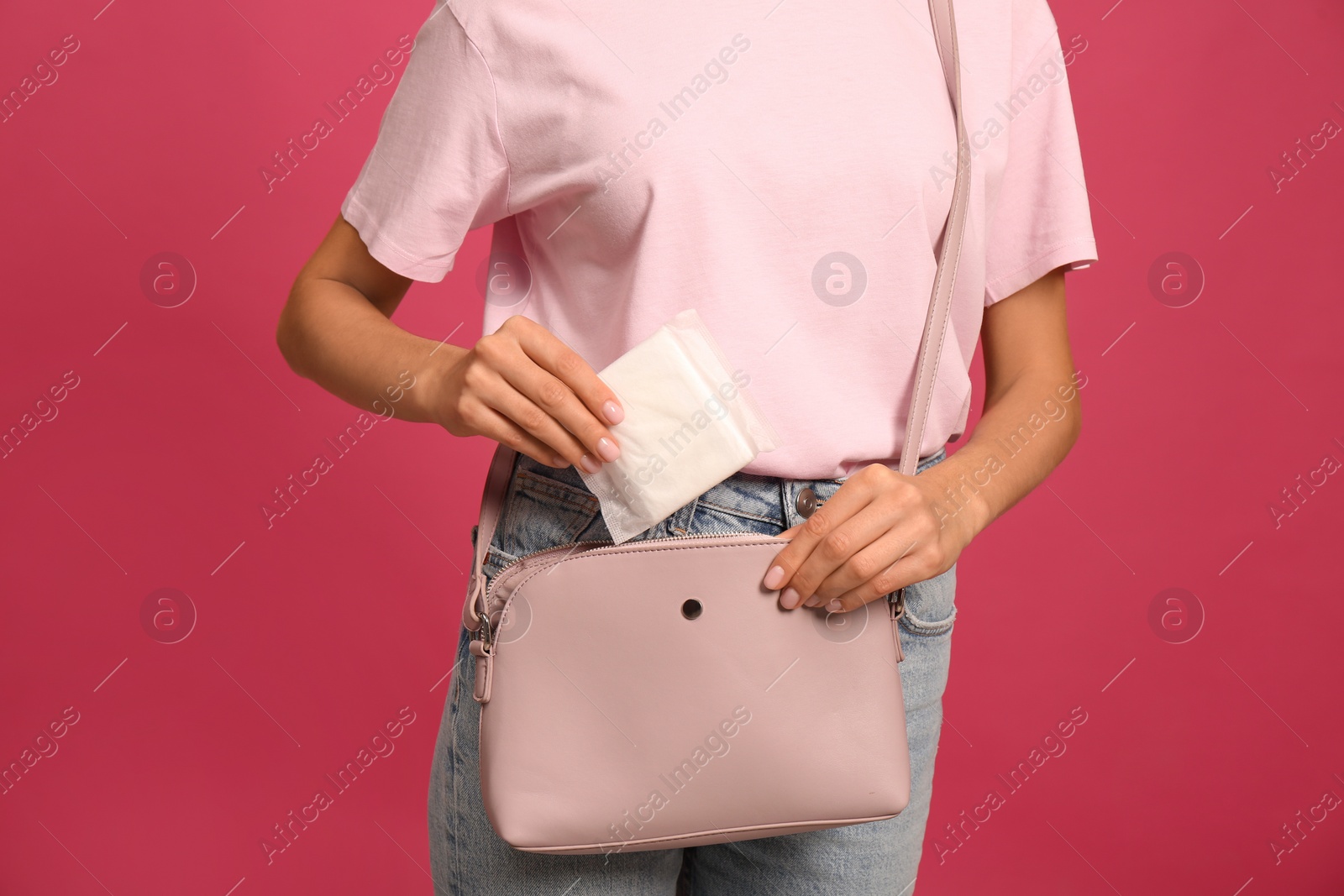 Photo of Young woman putting menstrual pad into purse on bright pink background, closeup