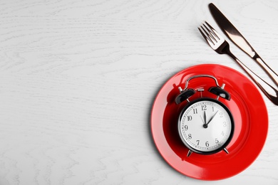 Photo of Alarm clock, plate and cutlery on white wooden table, flat lay with space for text. Diet regime