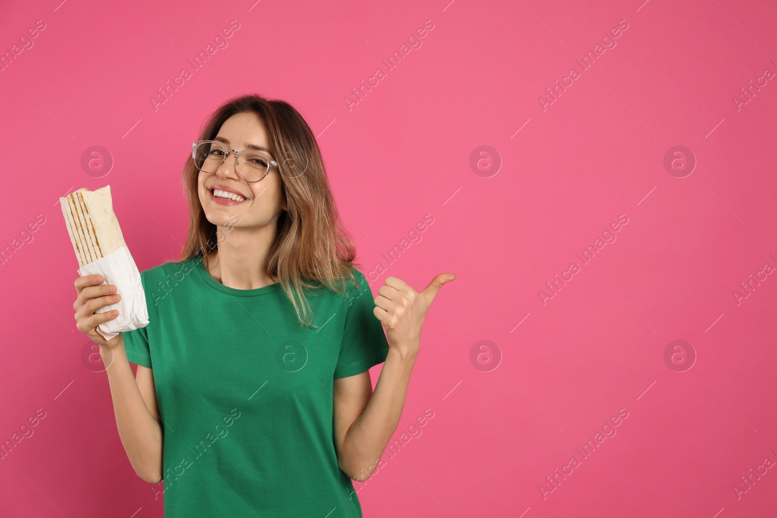 Photo of Young woman with delicious shawarma on pink background, space for text