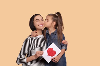 Happy woman with her cute daughter and handmade greeting card on beige background, space for text. Mother's day celebration