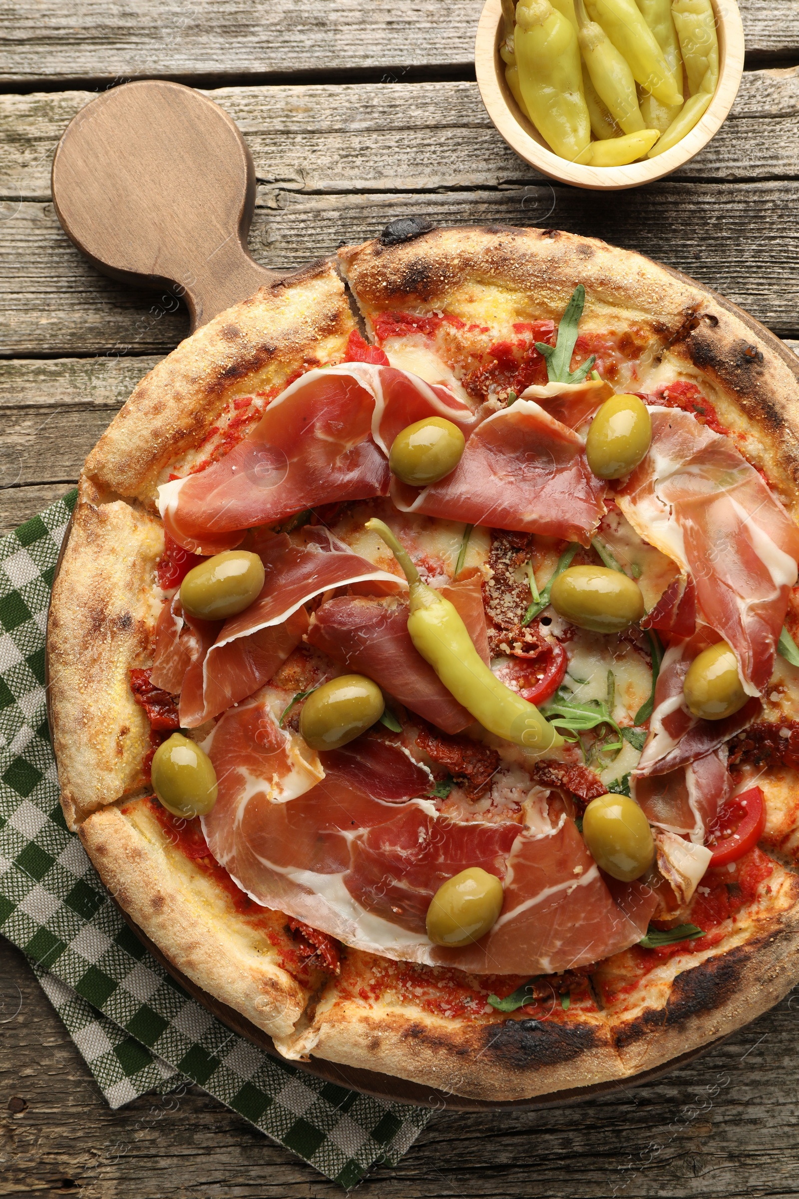 Photo of Tasty pizza with cured ham, olives, sun-dried tomato and peppers on wooden table, top view