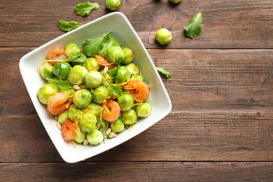 Photo of Bowl of delicious salad with Brussels sprouts and shrimps on wooden table, top view. Space for text