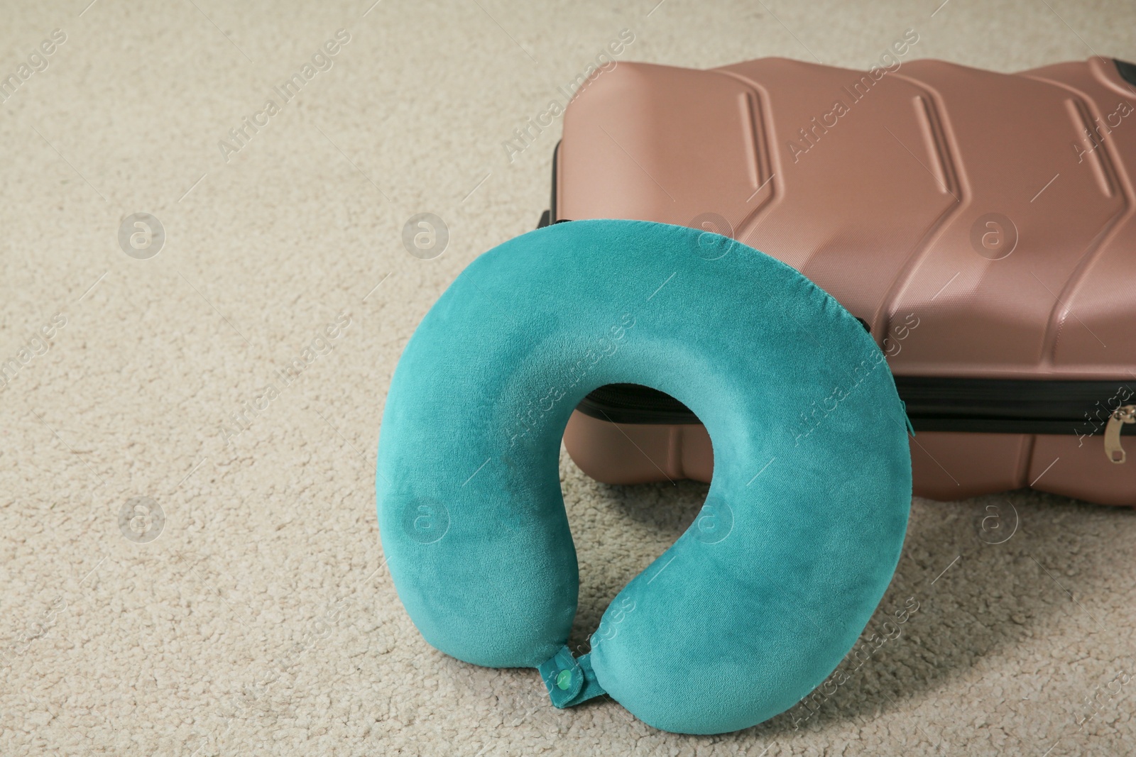 Photo of Turquoise travel pillow and suitcase on beige rug, space for text