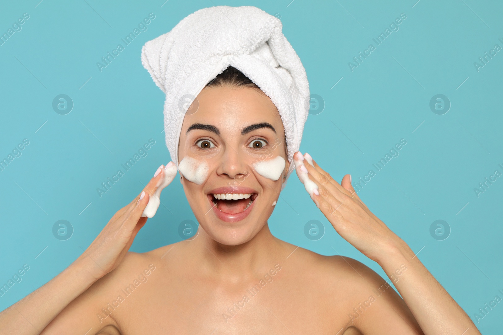 Photo of Emotional young woman washing face with cosmetic product on light blue background