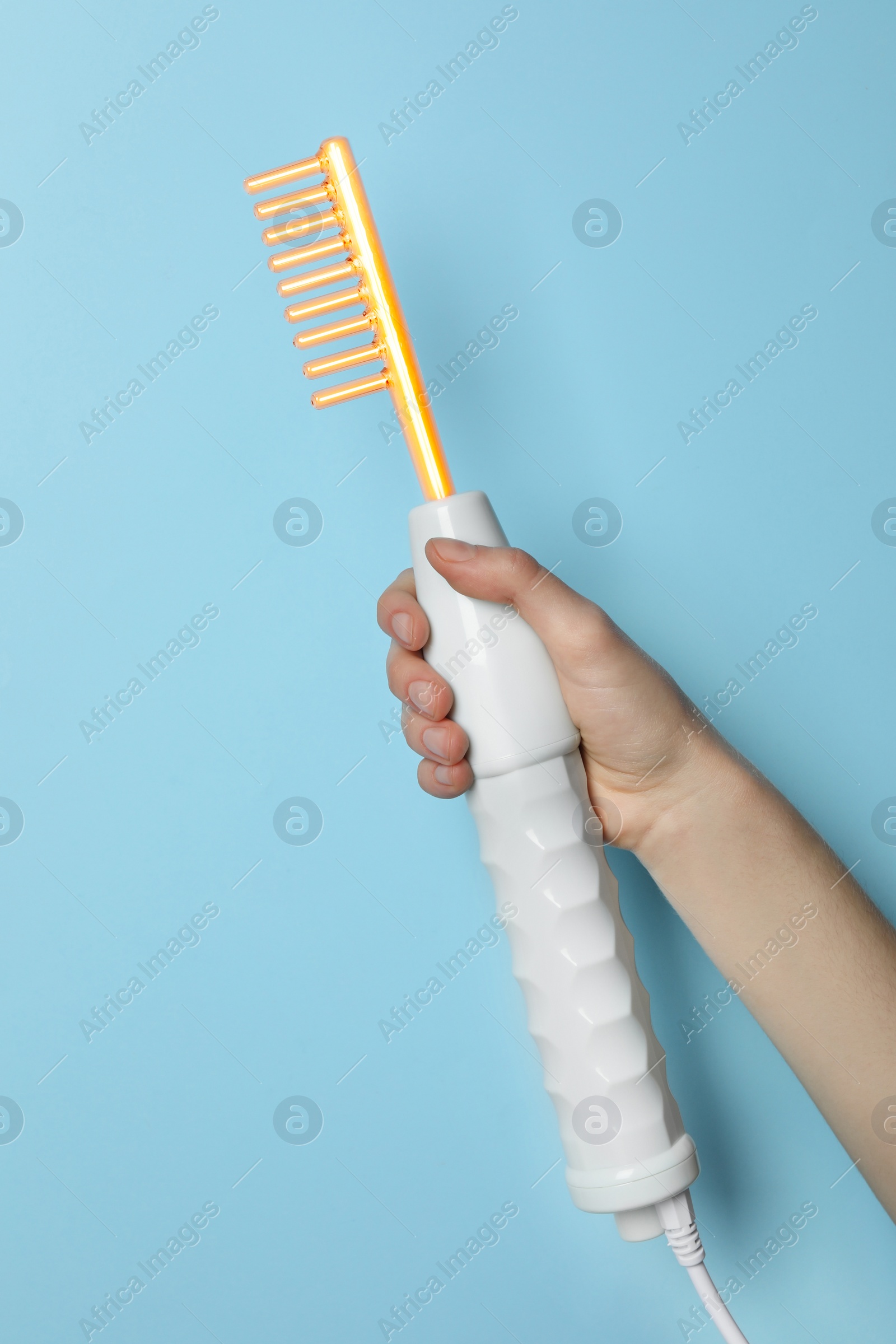 Image of Woman holding working high frequency darsonval device on light blue background, closeup