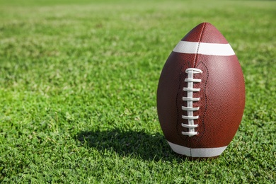 Photo of Ball for American football on fresh green field grass. Space for text