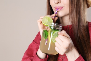 Woman drinking natural detox lemonade on beige background, closeup. Space for text