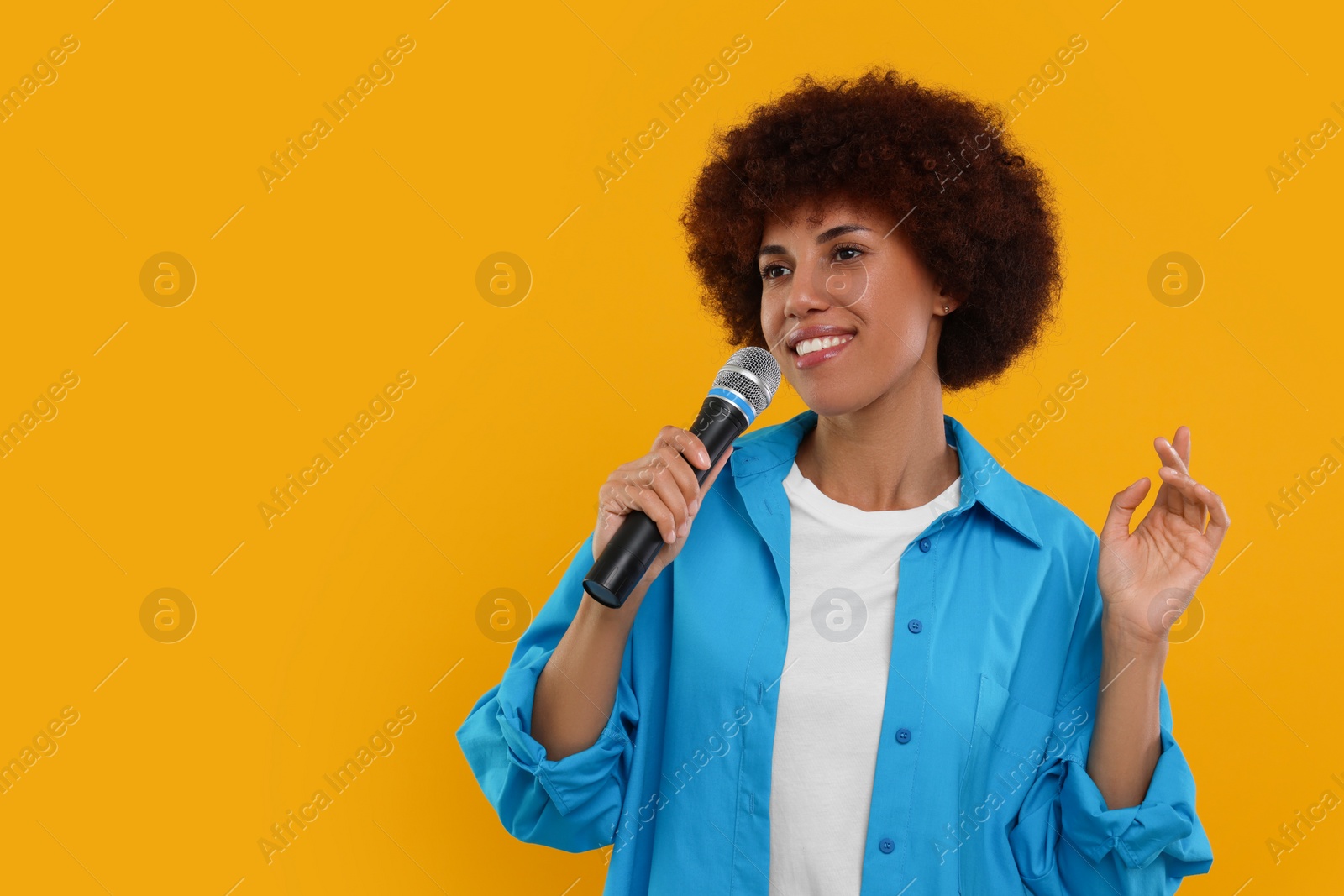 Photo of Curly young woman with microphone singing on yellow background, space for text