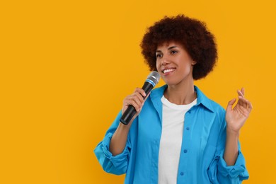 Curly young woman with microphone singing on yellow background, space for text