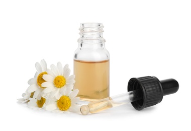 Chamomile flowers and cosmetic bottle of essential oil on white background