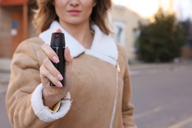 Young woman using pepper spray outdoors, closeup. Space for text