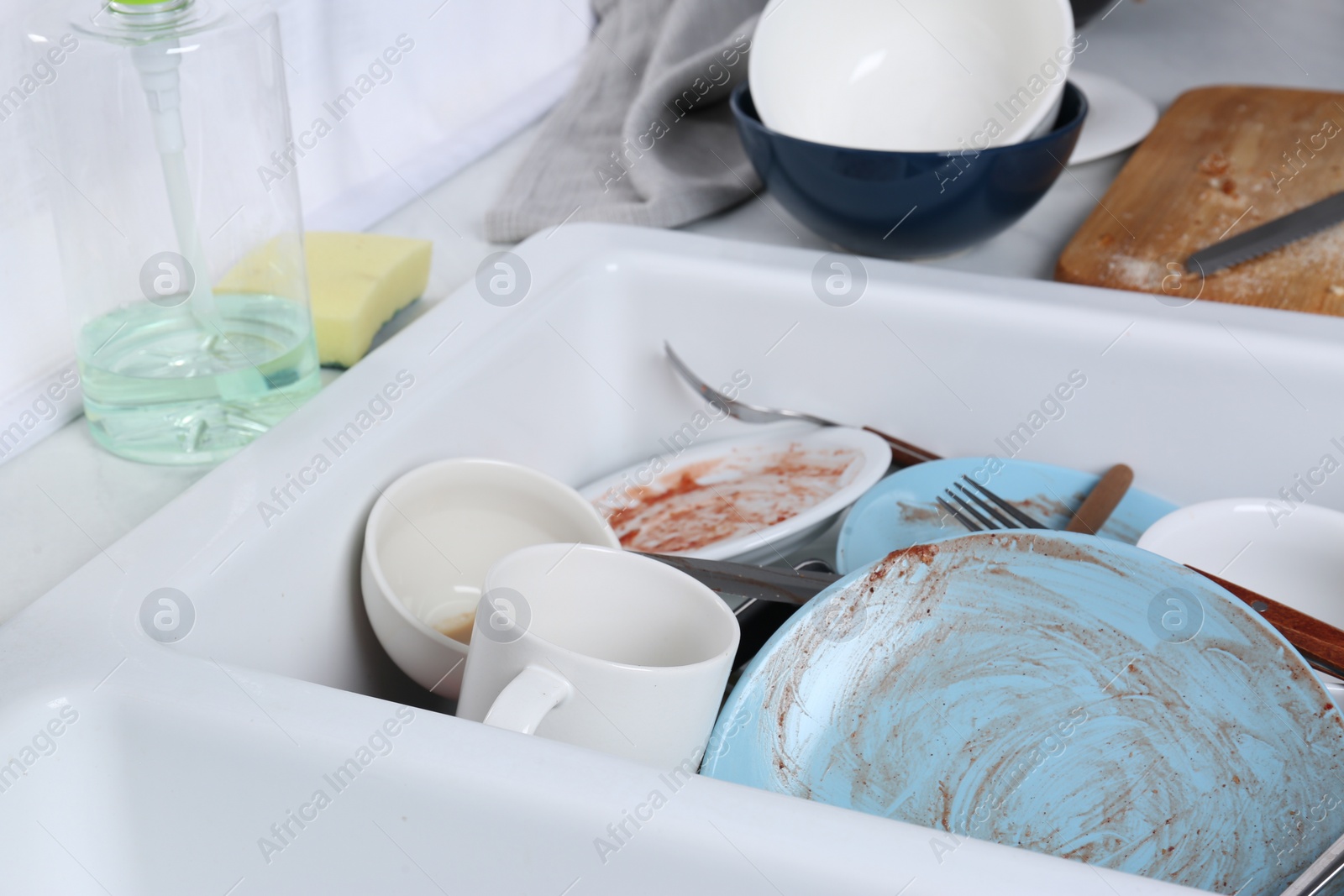 Photo of Sink with many dirty utensils and dishware in messy kitchen