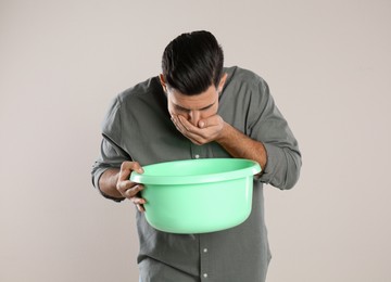 Man with basin suffering from nausea on beige background. Food poisoning