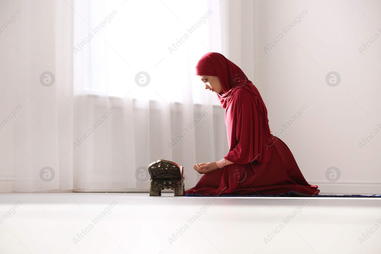 Photo of Muslim woman in hijab praying on mat indoors