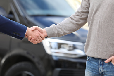 Photo of Salesman shaking hands with customer in modern auto dealership, closeup. Buying new car
