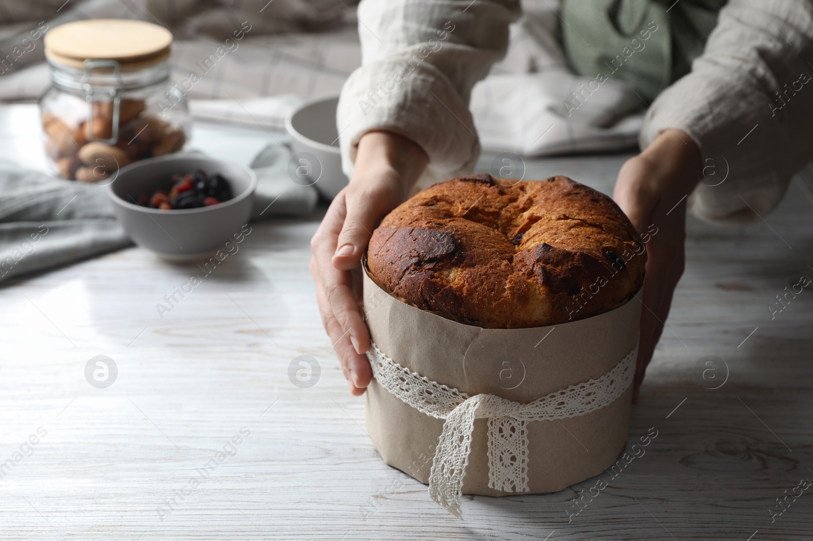 Photo of Woman holding delicious Panettone cake at white wooden table, closeup and space for text. Traditional Italian pastry