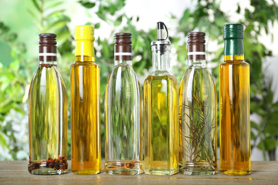 Photo of Different sorts of cooking oil in bottles on wooden table