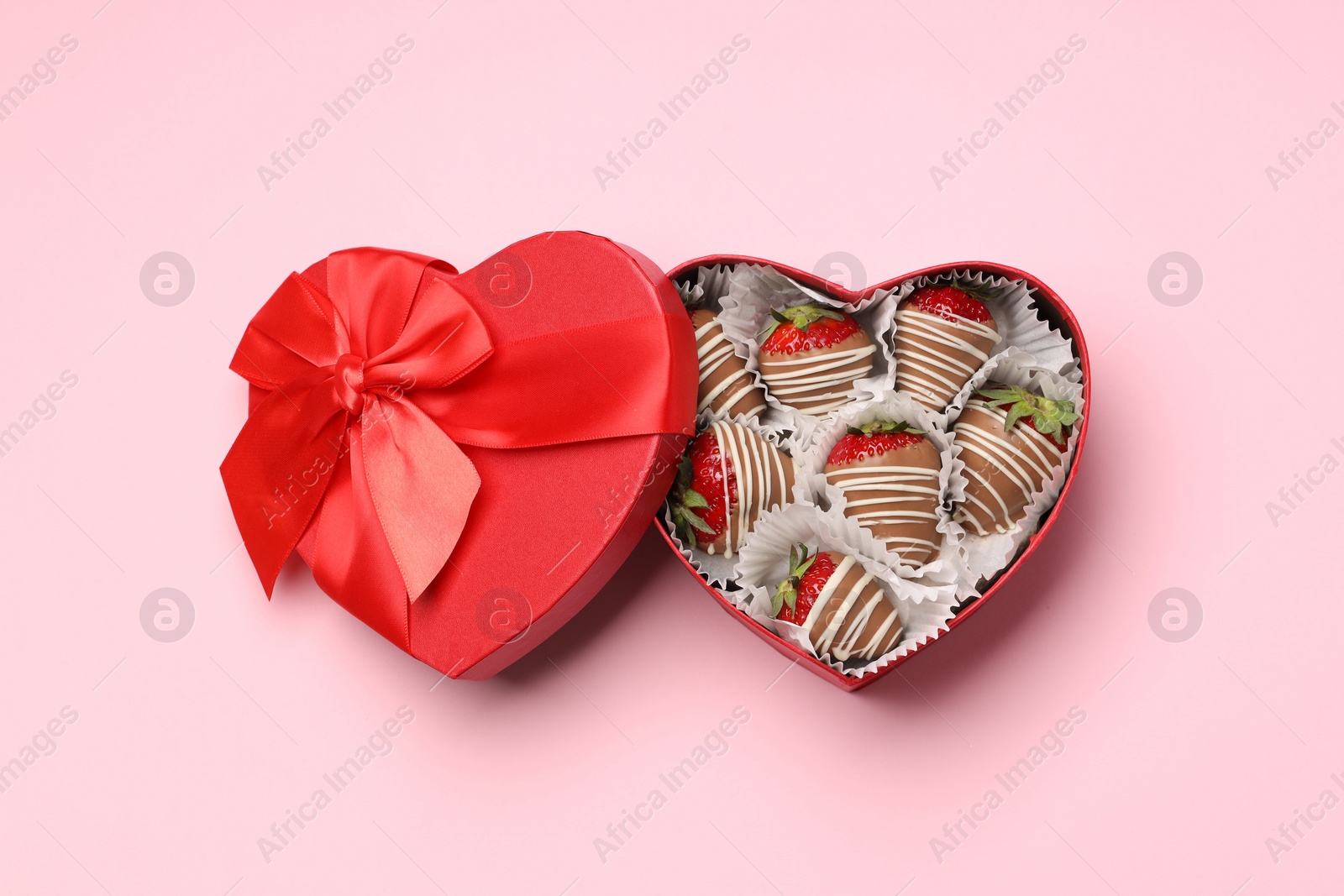 Photo of Heart shaped box with delicious chocolate covered strawberries on pink background, top view