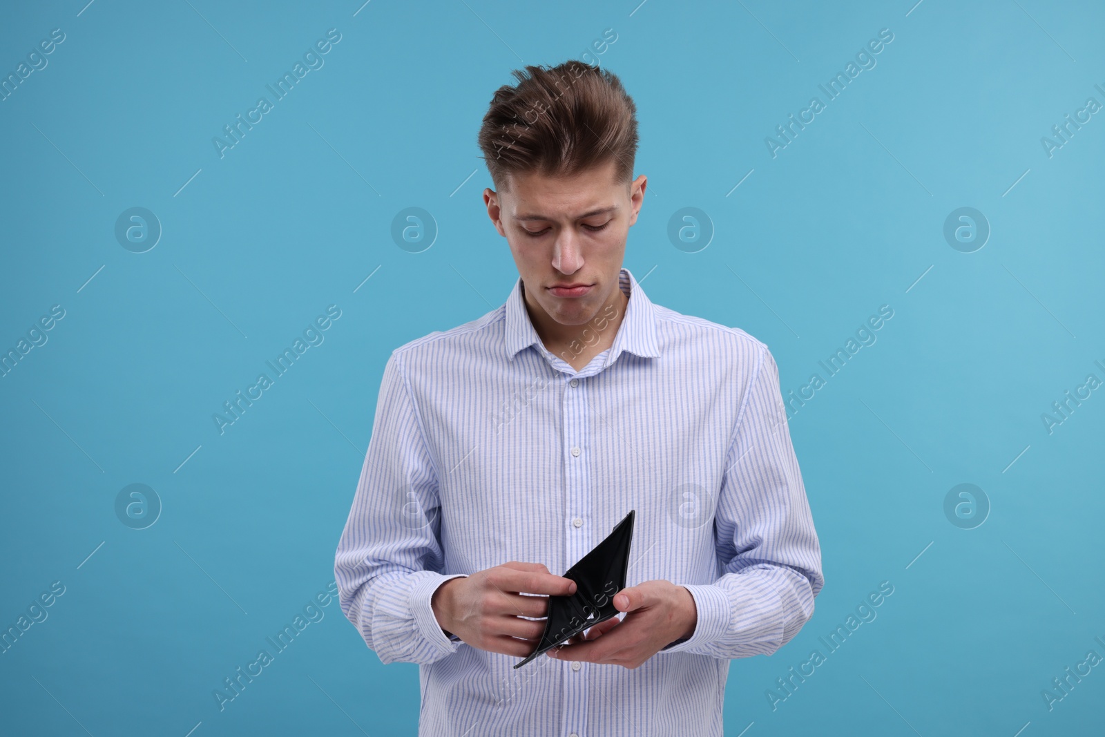 Photo of Upset man looking into empty wallet on light blue background