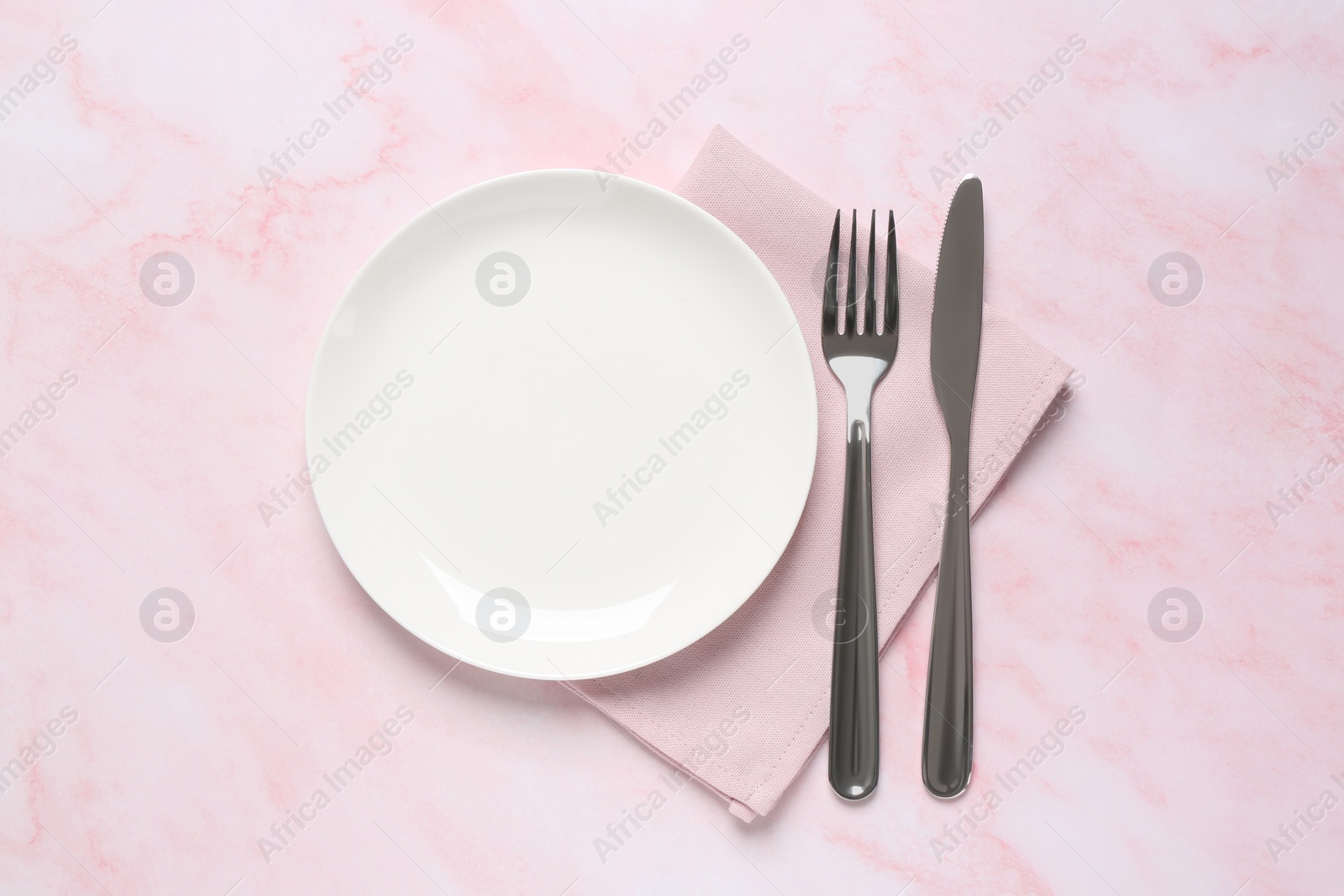 Photo of Clean plate and shiny silver cutlery on light pink marble table, flat lay