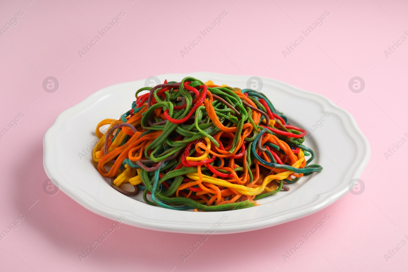 Photo of Plate of spaghetti painted with different food colorings on pink background