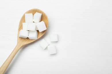 Many sugar cubes and wooden spoon on white table, top view. Space for text