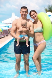 Happy parents with little baby in swimming pool on sunny day, outdoors