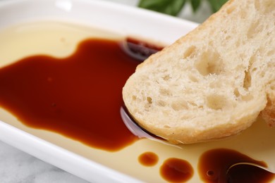Photo of Bowl of organic balsamic vinegar with oil served with bread slice on white table, closeup