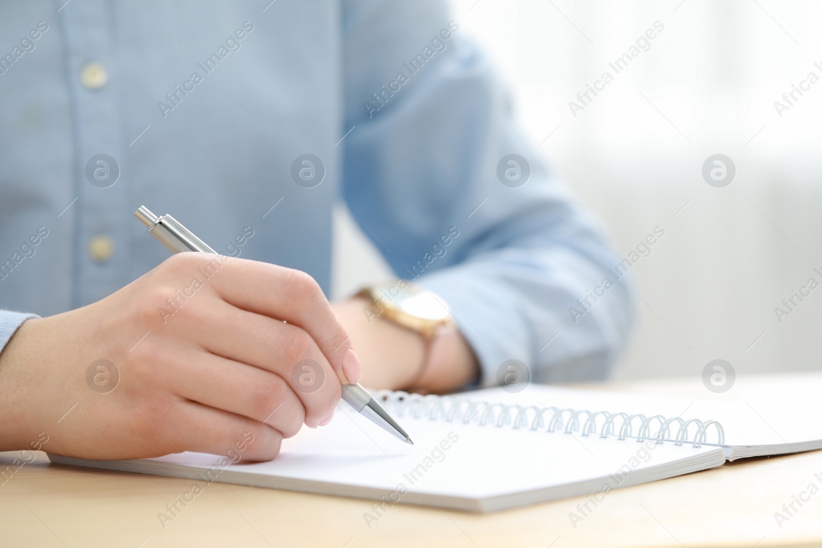 Photo of Woman writing in notebook at wooden table, closeup