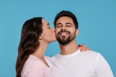 Photo of Woman kissing her smiling boyfriend on light blue background