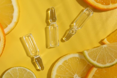 Skincare ampoules with vitamin C and citrus slices on yellow background, flat lay