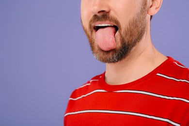 Photo of Man showing his tongue on violet background, closeup. Space for text