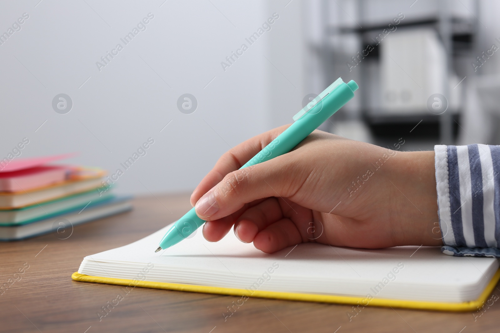 Photo of Woman writing in notebook at wooden table indoors, closeup